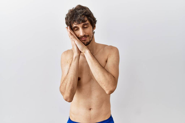 Young hispanic man standing shirtless over isolated, background sleeping tired dreaming and posing with hands together while smiling with closed eyes.  - Photo, Image