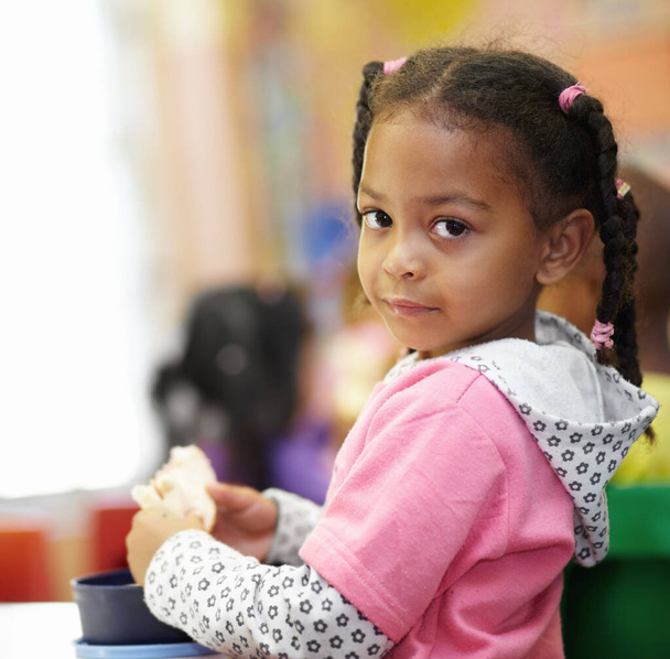 Питание важно для ее роста. Портрет милой маленькой девочки, поедающей сэндвич в классе - Фото, изображение