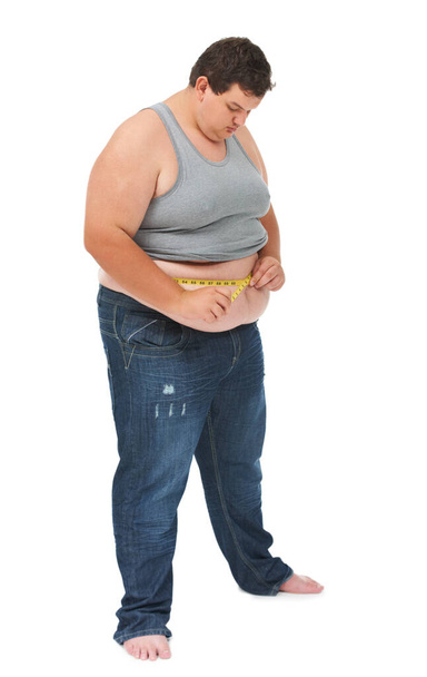 Auf sein Gewicht achten. Ein fettleibiger junger Mann misst seine Taille mit einem Maßband vor weißem Hintergrund - Foto, Bild