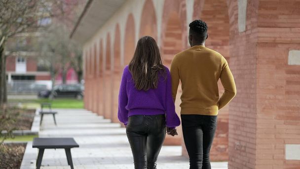 Giovane coppia interrazziale camminare insieme al di fuori tenendosi per mano - Foto, immagini