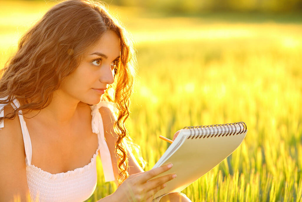 Mujer dibujando en un cuaderno en un campo al atardecer - Foto, imagen