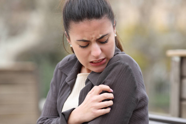 Stressed woman scratching itchy arm in a park - Photo, Image
