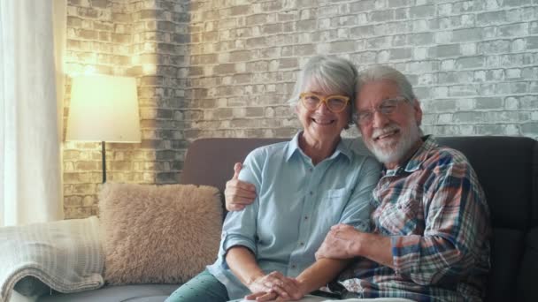 Bonito e belo casal de idosos sorrindo e olhando para a câmera se divertindo em casa juntos. Idosos sentados no sofá desfrutando e relaxando. - Filmagem, Vídeo