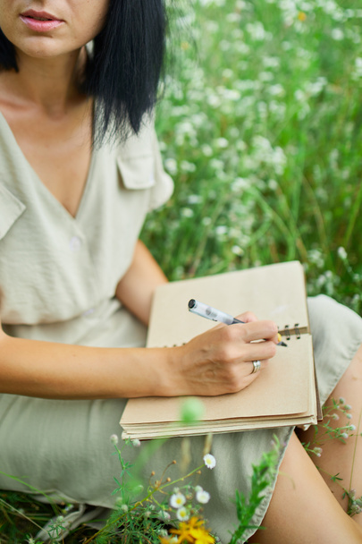 Žena s perem psaní nebo malování, rukopis na notebooku na květinové louce, na venkově, na poli v letní den na louce, cítit přírodu, relaxovat, sám cestovat. - Fotografie, Obrázek