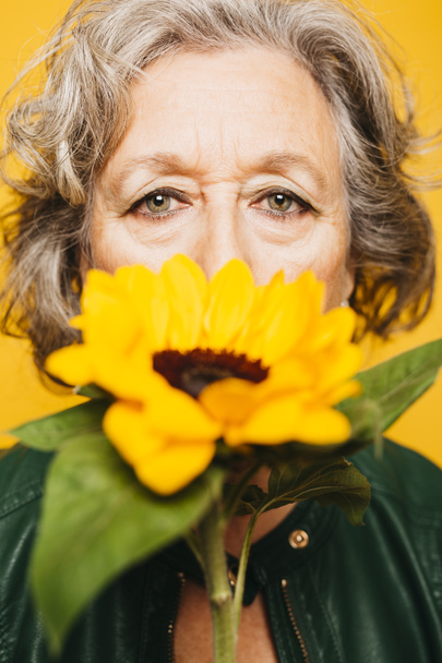 Portrait d'une femme âgée avec un tournesol sur fond jaune - Photo, image
