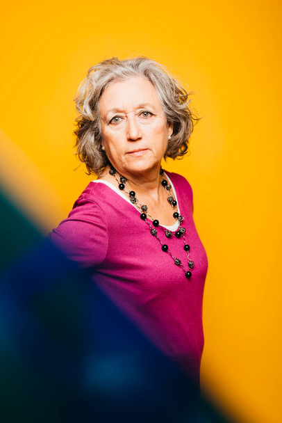 Porträt einer Seniorin mit rosa Pullover vor gelbem Hintergrund - Foto, Bild