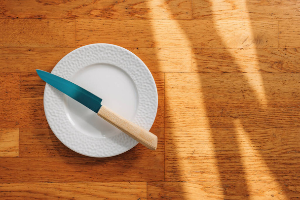 Kitchen knife and empty plate on wooden background, top view - Fotó, kép