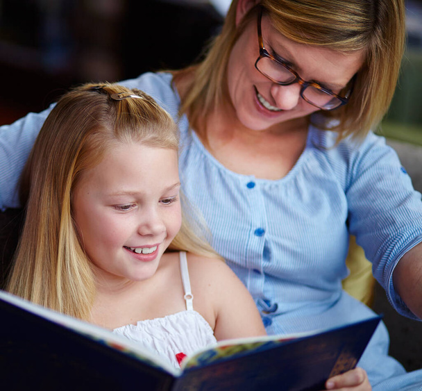 A kedvenc könyvem. Egy csinos fiatal lány ül az anyja mellett, miközben könyvet olvasnak. - Fotó, kép