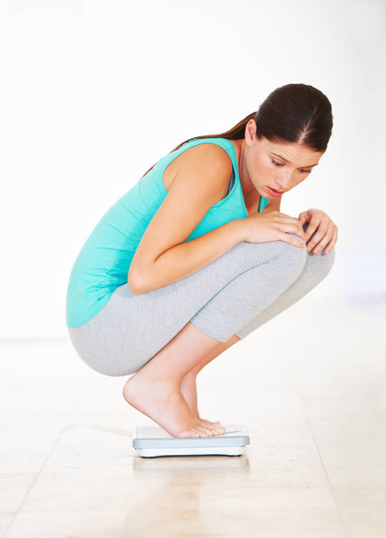 Ive lost so much weight already...A young woman crouching on a scale and looking shocked - Foto, imagen