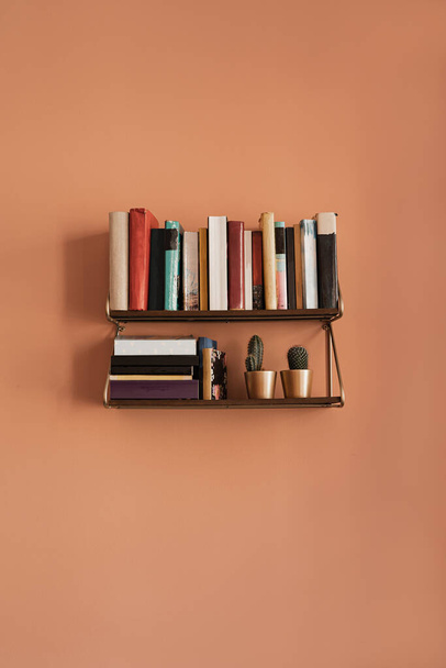 Books stack on hanging shelf. Coral peach wall background. Aesthetic minimal interior design. Reading, education concept with bookshelf - Photo, Image
