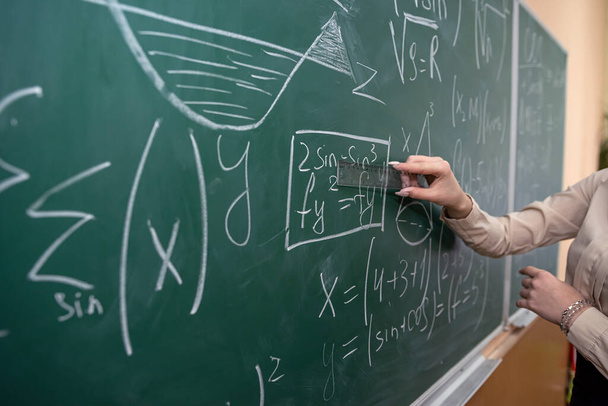 γυναικείο χέρι με κιμωλία και να γράψει μαθηματικό τύπο στον πίνακα. έννοια της εκπαίδευσης. τάξη - Φωτογραφία, εικόνα