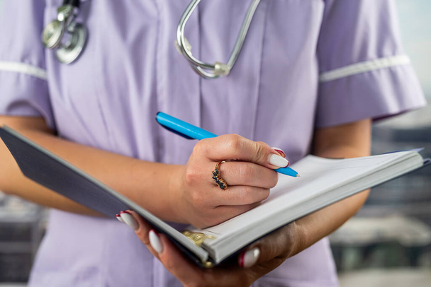 close-up photo of a nurse in uniform holding a journal and taking notes in a hospital. concept of medicine and health - Photo, Image