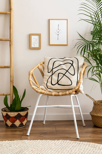 Boho and cozy interior of living room with design rattan armchair, pillows, mock up poster frame, plant, bamboo ladder, decoration and personal accessories. Stylish home decor. Template. - 写真・画像