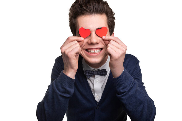 Silly young male in smart casual clothes covering eyes with small hearts and smiling while expressing love against white background - Fotoğraf, Görsel