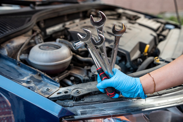 Close-up of an old catalytic converter in the hand of a car mechanic and holding a wrench to remove the part in the engine compartment of a car. garage service and maintenance concept - Photo, Image