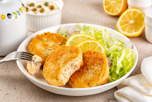 Eating Fish cakes or burger, or putties. Made from ground perch and tuna with herbs, breaded and fried, served with iceberg salad, lemon slices. - Photo, Image