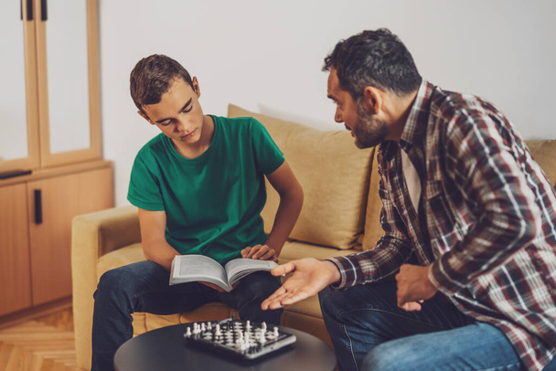 Отец и сын играют в шахматы дома. Мальчик изучает шахматы. - Фото, изображение