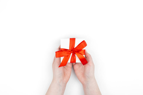 Geschenkkarton in roter Schleife in weiblichen Händen auf weißem Hintergrund isoliert, Ansicht von oben. - Foto, Bild