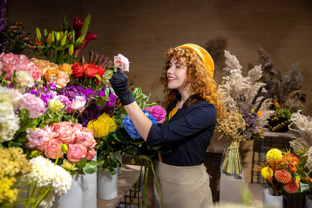 In a flower shop. Smiling curly-haired florist with flowers - Foto, afbeelding