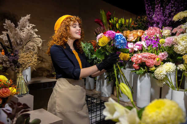Lovely florist. Ginger young woman in a flower shop looking romantic and contented - Foto, Bild