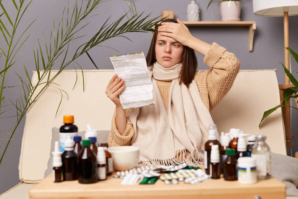 Image of unhealthy ill Caucasian woman reading instructions before taking medication, suffering terrible headache, touched her forehead, having high temperature. - Foto, imagen