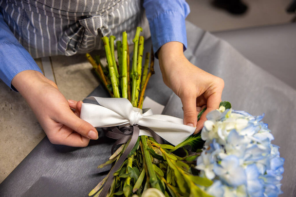 Flower shop. Close up of florist tying a ribbon on a bouquet - Foto, afbeelding