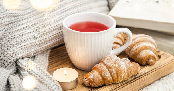 Sıcak kompozisyon, bir fincan kırmızı çay, bir mum, bir kruvasan ve bir örgü elementi.... - Fotoğraf, Görsel