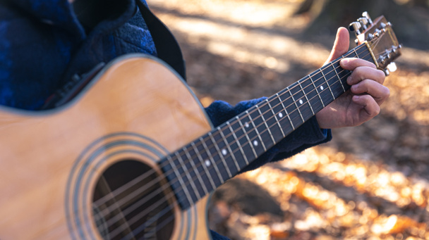Close-up, een man speelt een akoestische gitaar in het bos tijdens het koude seizoen. - Foto, afbeelding
