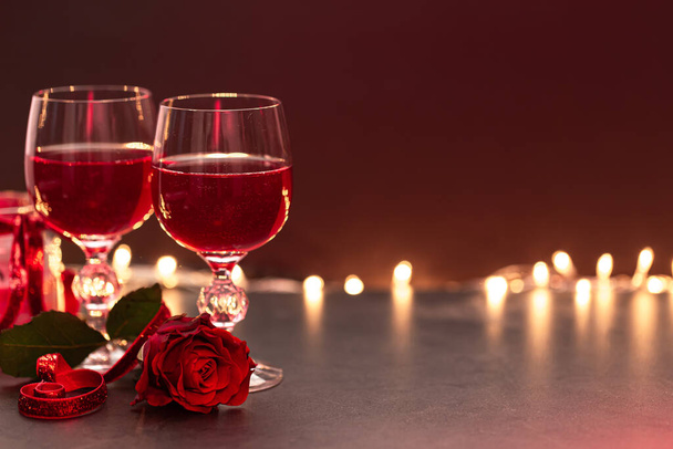 Dwie szklanki wina i czerwona róża na rozmytym tle z bokeh, przestrzeń kopiowania. - Zdjęcie, obraz