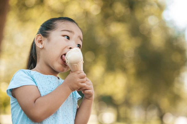 Tasty ice-cream. Cute little girl eating ice-cream and looking contented - Фото, изображение