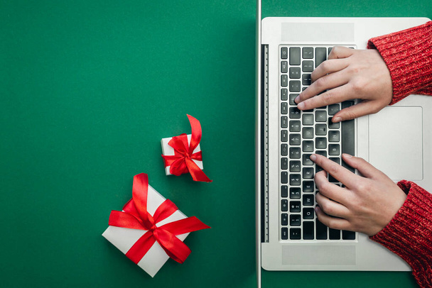 Geschenkschachteln und Laptop auf grünem Hintergrund, Frau beim Online-Weihnachtseinkauf, Ansicht von oben. - Foto, Bild