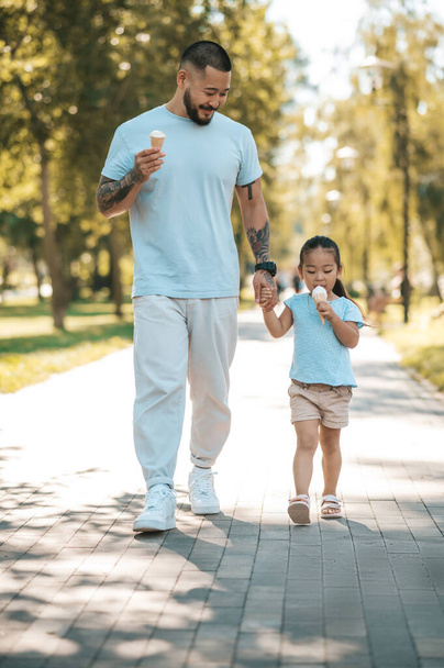 Eating ice-cream. Young dad and his daughter eating ice-cream and looking enjoyed - 写真・画像