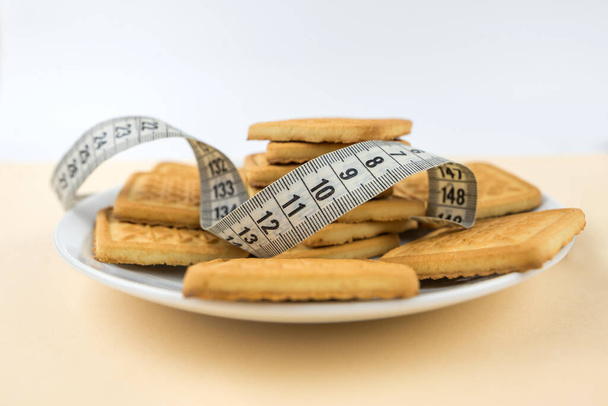 cookies in a plate and a measuring tape. cookies in a white plate. Around it is a measuring tape folded into a ring, which symbolizes the harm of sweets for the figure and the size of the waist. - Photo, Image