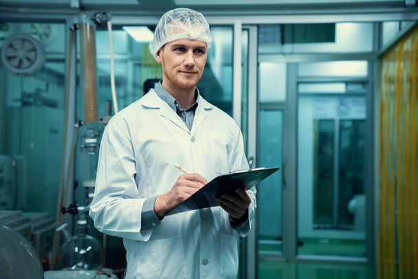 Apothecary scientist using a clipboard and pen to record information from a CBD oil extractor and a scientific machine used to create medicinal cannabis products. - Photo, image