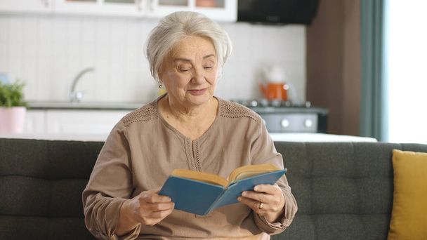 Starsza kobieta w spokojnym domu czyta książkę, ciesząc się wolnym czasem. Szczęśliwi starzy ludzie, koncepcja emerytki. Pojęcie miłości do czytania książek. - Zdjęcie, obraz