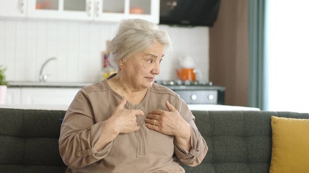 Senior gray haired woman wearing casual clothes, skeptical and nervous, disapproving expression on face. Negative person. Grumpy old woman sitting on sofa at home. - Photo, Image