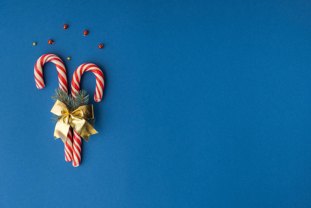 Gestreifte rote Zuckerstangen mit Weihnachtsbaumspielzeug auf blauem Hintergrund. Festlicher Weihnachtshintergrund mit Freiraum für Grußworte. Frohe Weihnachten und ein gutes neues Jahr - Foto, Bild