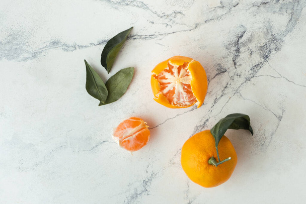 Πορτοκαλί ζουμερές φέτες μανταρινιού και καθαρισμένα μανταρίνια σκορπισμένα στο λευκό μαρμάρινο φόντο. Επίπεδη. Αντιγραφή χώρου. Φρέσκα φρούτα πλούσια σε βιταμίνες του καλοκαιριού σε ένα ψάθινο καλάθι - Φωτογραφία, εικόνα