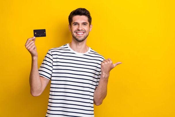 Photo of cheerful nice man toothy smile hold debit card direct finger empty space isolated on yellow color background. - Photo, Image