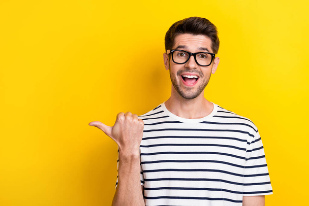 Photo of astonished cheerful man open mouth indicate thumb finger empty space isolated on yellow color background. - 写真・画像