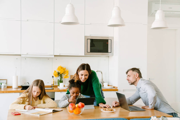 Happy family on cozy kitchen at home, mother and working father helping their daughters with homework - Valokuva, kuva