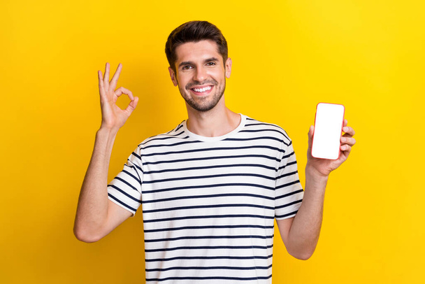 Photo of positive handsome guy show okey symbol empty space telephone screen isolated on yellow color background. - Photo, Image
