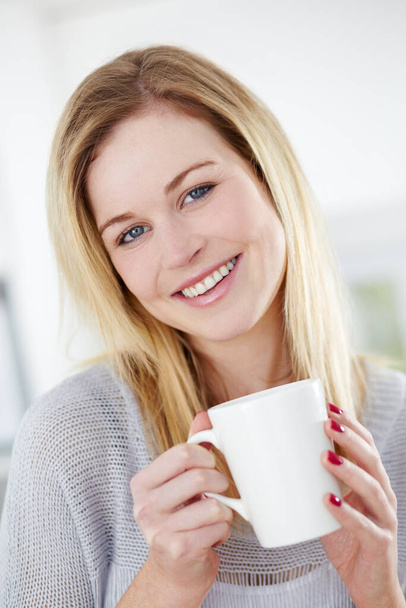 She enjoys a refreshing cup of tea. Cute young woman drinking a cup of coffee with a smile - Zdjęcie, obraz