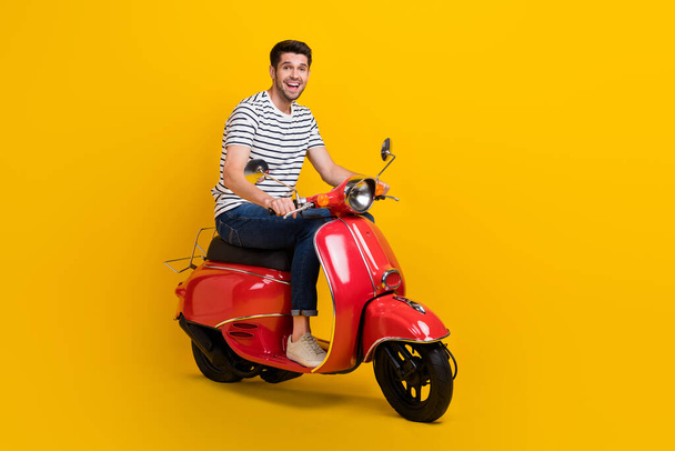 Full length photo of pretty impressed guy dressed striped t-shirt riding moped empty space isolated yellow color background. - Foto, immagini