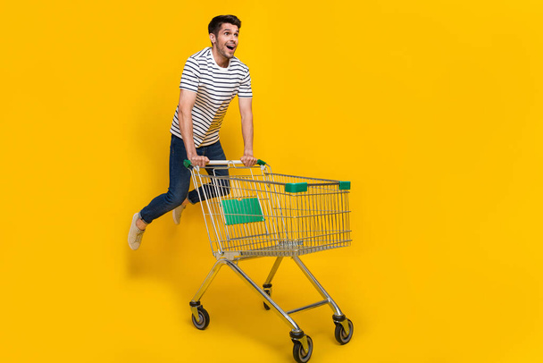 Full length photo of funky impressed man wear white t-shirt jumping high enjoying retail shopping isolated yellow color background. - 写真・画像