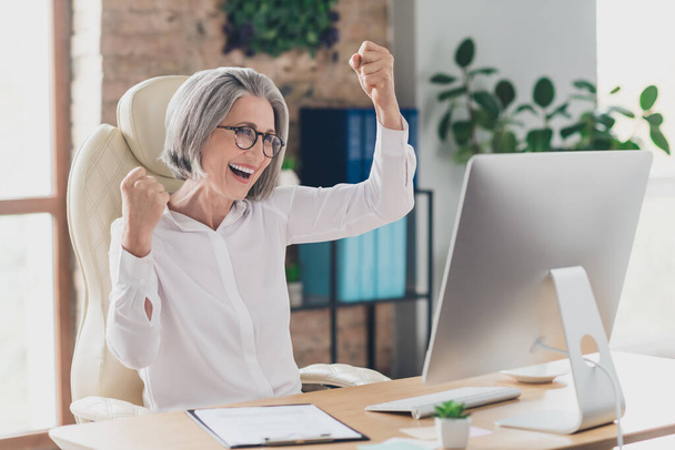 Portrait of delighted excited person sit chair raise fists luck attainment accomplishment workstation indoors. - Fotoğraf, Görsel