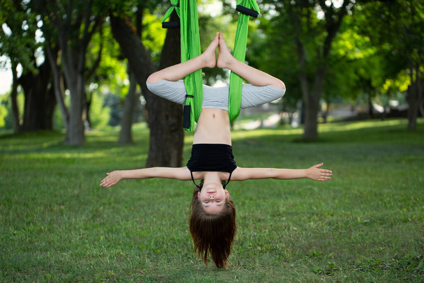 Little girl doing yoga exercises with a hammock in the park - Foto, Imagen