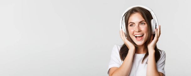 Nahaufnahme eines schönen, glücklichen Mädchens, das lächelnd Musik in drahtlosen Kopfhörern hört. - Foto, Bild