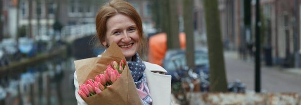 happy smiling girl holding a bouquet of tulips standing on a street of Amsterdam. The Netherland - Foto, immagini