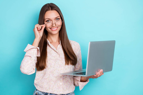 Photo of optimistic millennial woman hold laptop wear shirt spectacles isolated on blue color background. - 写真・画像